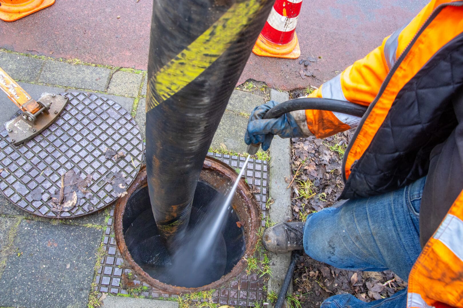 Sewer worker cleaning manhole with pressure hose