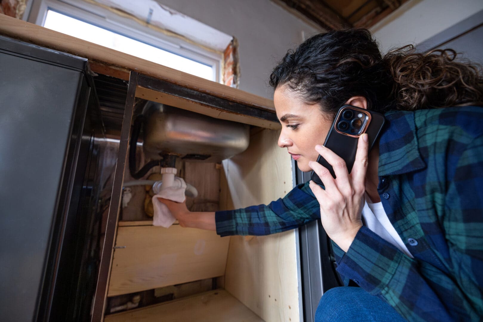 Woman inspecting under sink while on phone.
