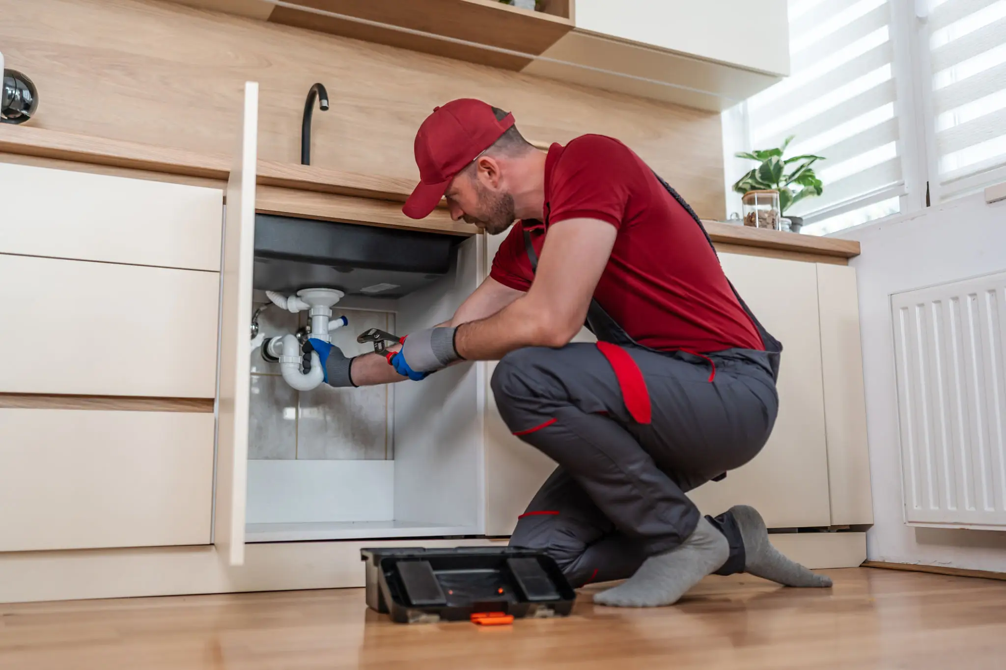 Plumber providing emergency plumbing services under a kitchen sink.